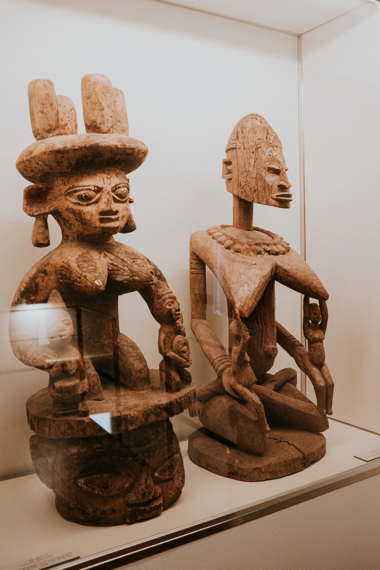 Se observan dos esculturas africanas de madera sobre una vitrina en una sala de exposición.