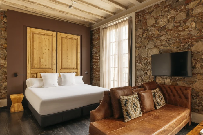 Se ve una cama doble, un sillón de cuero y una pared de ladrillo con una televisión y una ventana con cortinas.