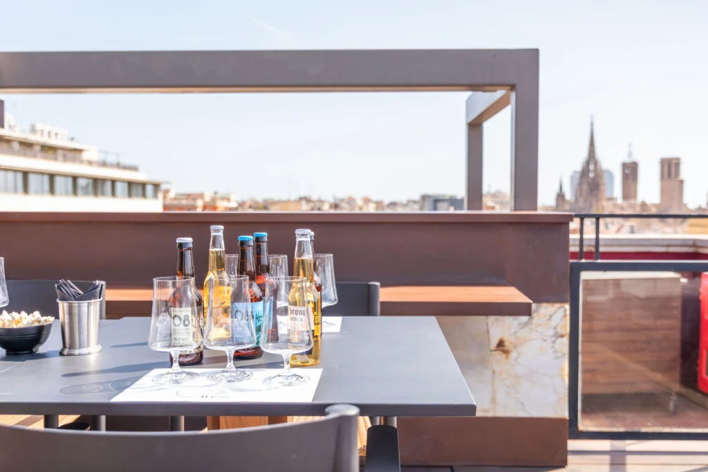 You can see a table with bottles and glasses on a terrace, with a railing and a chimney in the background.