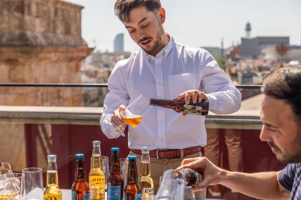 A man serves drinks from a table with bottles and glasses on an outdoor terrace.