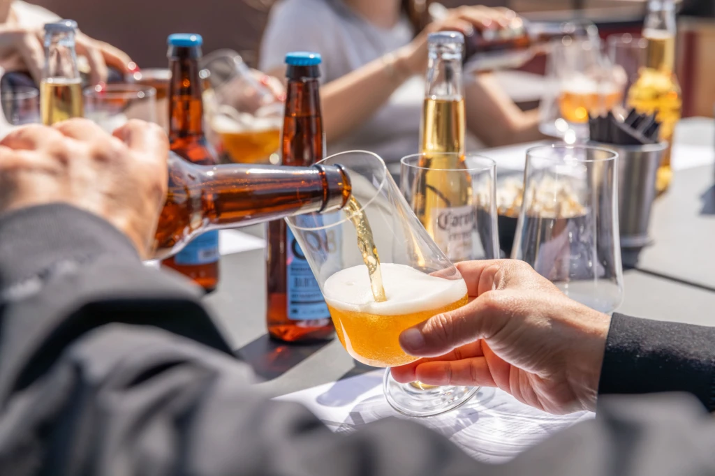 Diverse persone brindano con bicchieri di birra attorno a un tavolo con bottiglie e bicchieri.