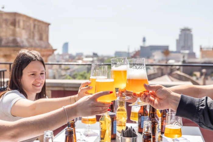 Più persone brindano con i bicchieri di birra su una terrazza, con bottiglie sul tavolo.