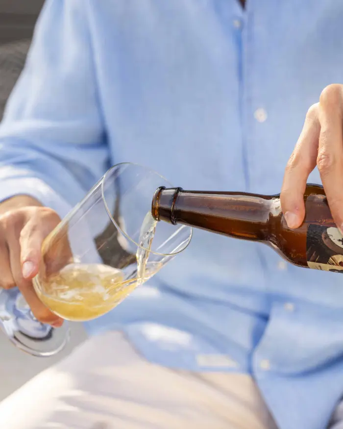 Plusieurs personnes portent un toast avec des verres de bière sur une terrasse, avec des bouteilles sur la table.