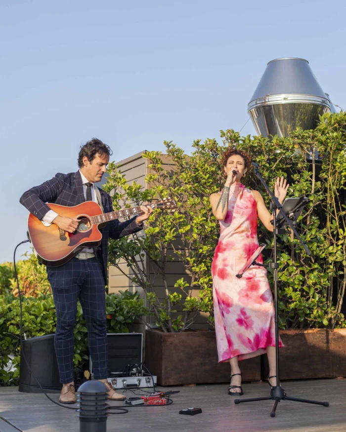 On an outdoor stage, two musicians perform with a singer and an acoustic guitar.
