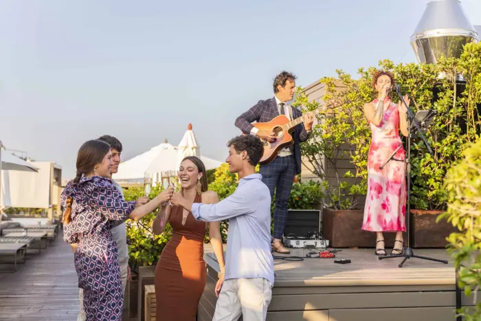 On an outdoor stage, two musicians perform with a singer and an acoustic guitar.