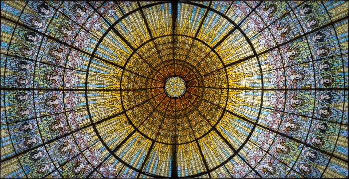 Descriu una vidriera modernista circular amb motius florals i un marc negre al sostre.