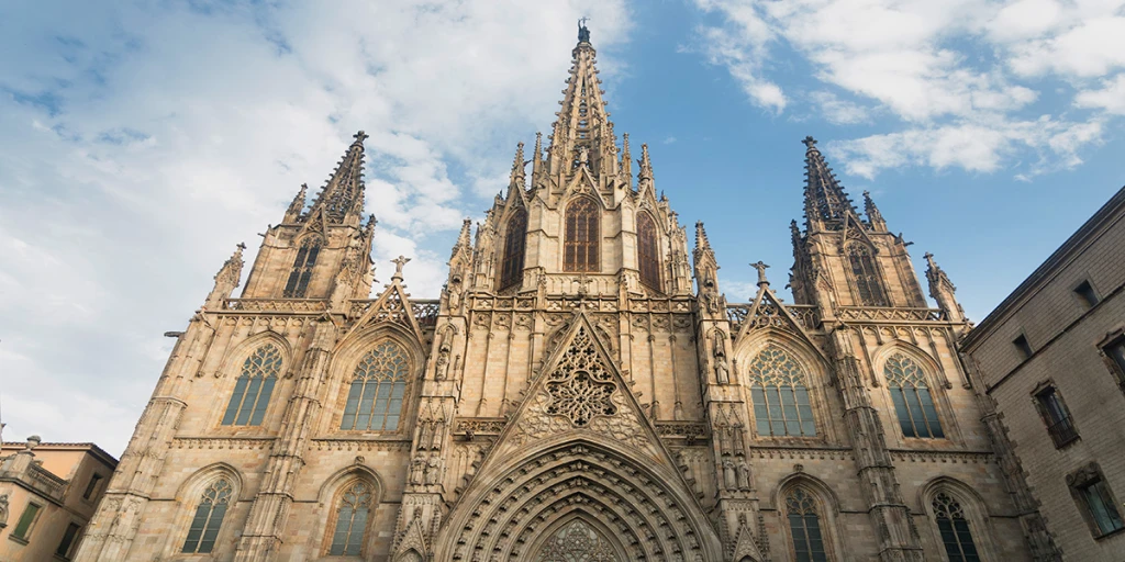 Es veu la façana d’una catedral gòtica amb torres altes i arcs ornamentats sota un cel ennuvolat.