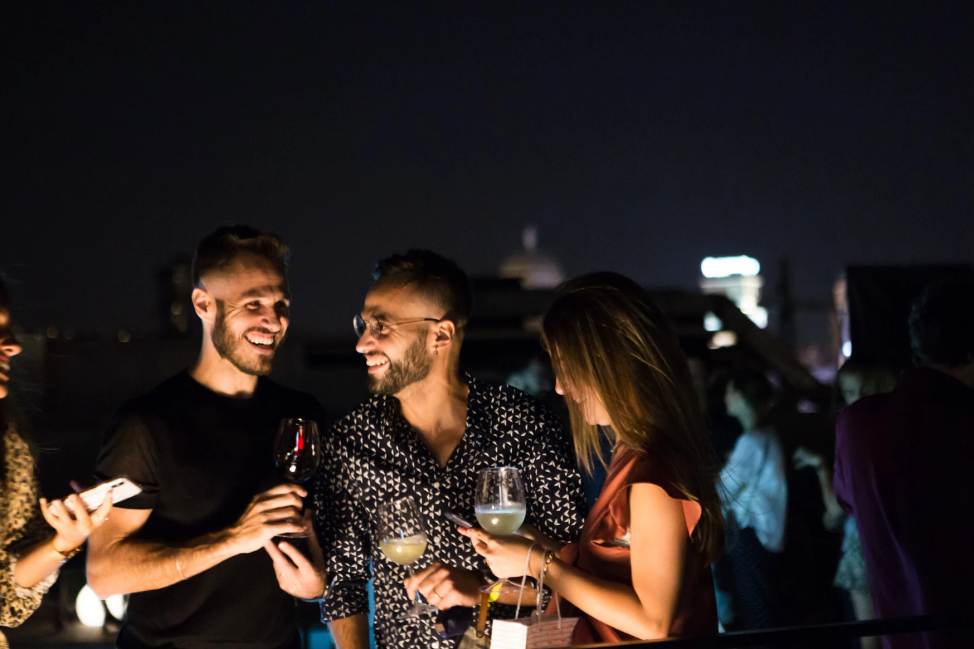 Plusieurs personnes trinquent avec des verres lors d’un événement social en plein air, le soir.