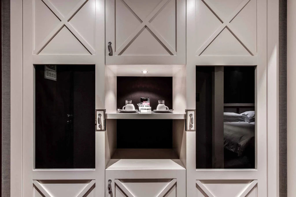 On voit un mur avec une niche décorative et deux portes ouvertes laissant apparaître des lits à l’intérieur.