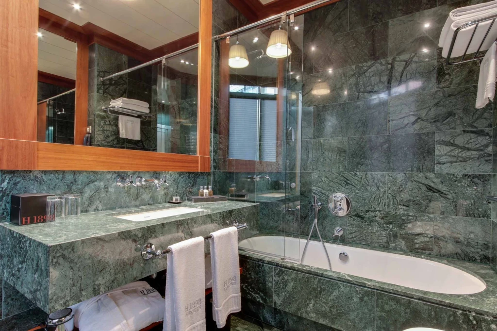 On voit une baignoire ovale, une douche en verre et un lavabo dans une salle de bain aux murs en pierre.