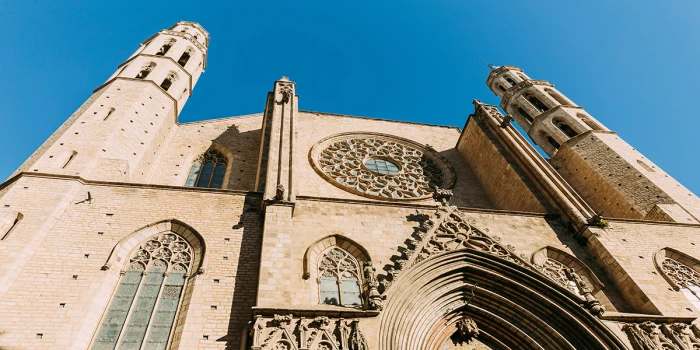 Si vede la facciata di un edificio storico con archi in pietra e due torri sotto un cielo azzurro.