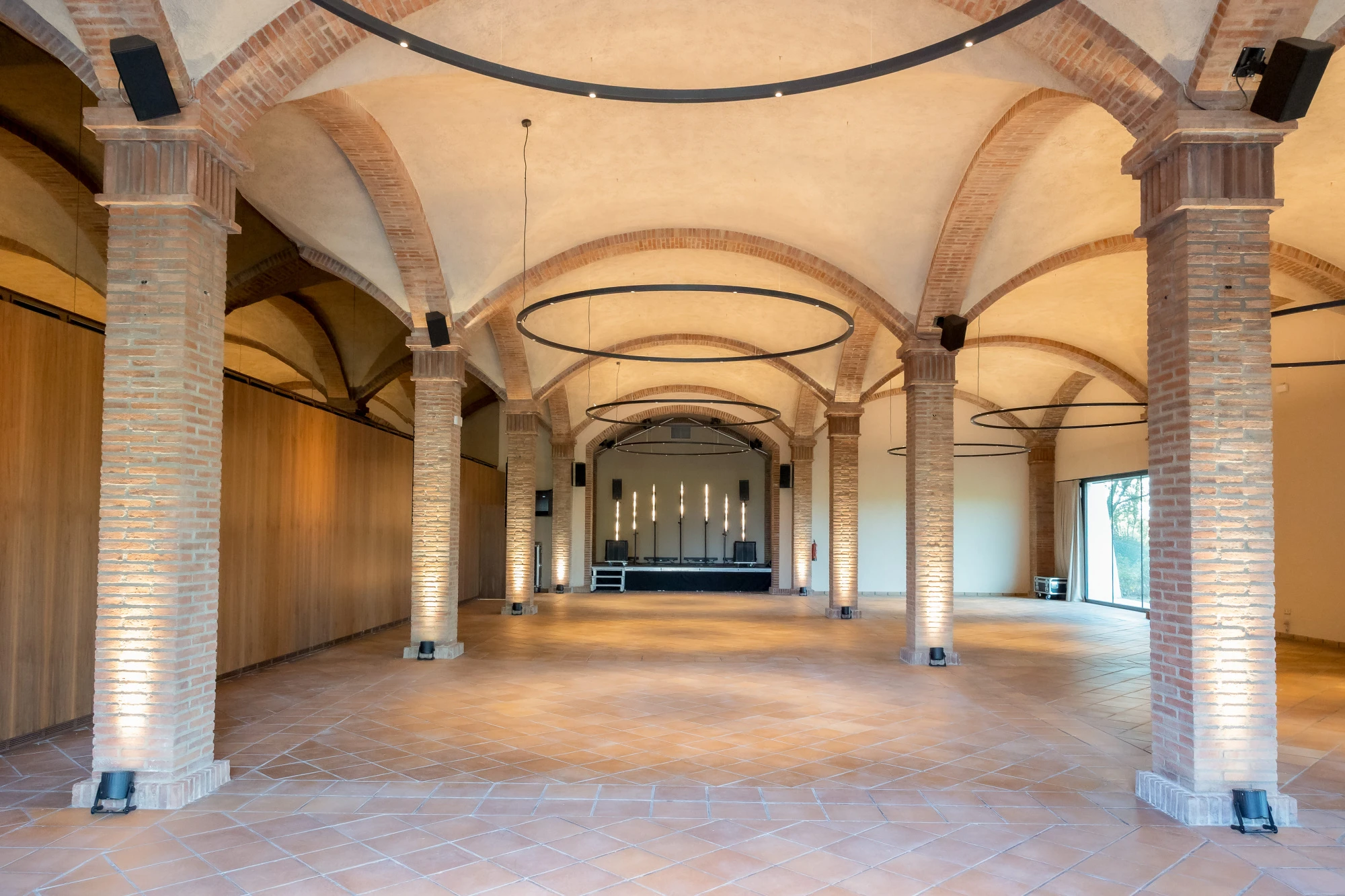 El pasillo interior muestra arcos de ladrillo, columnas y suelo de piedra bajo lámparas colgantes.