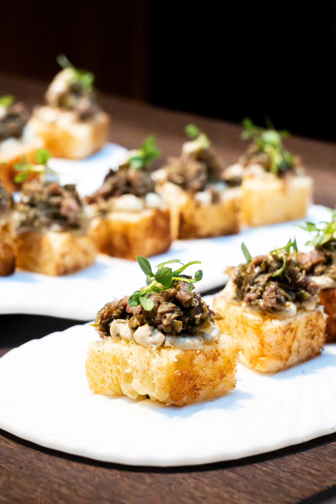 Una pieza de brioche tostado con una capa de tartar de anchoa y alcaparra, presentada de manera apetitosa y elegante, ideal para un aperitivo en un hotel.
