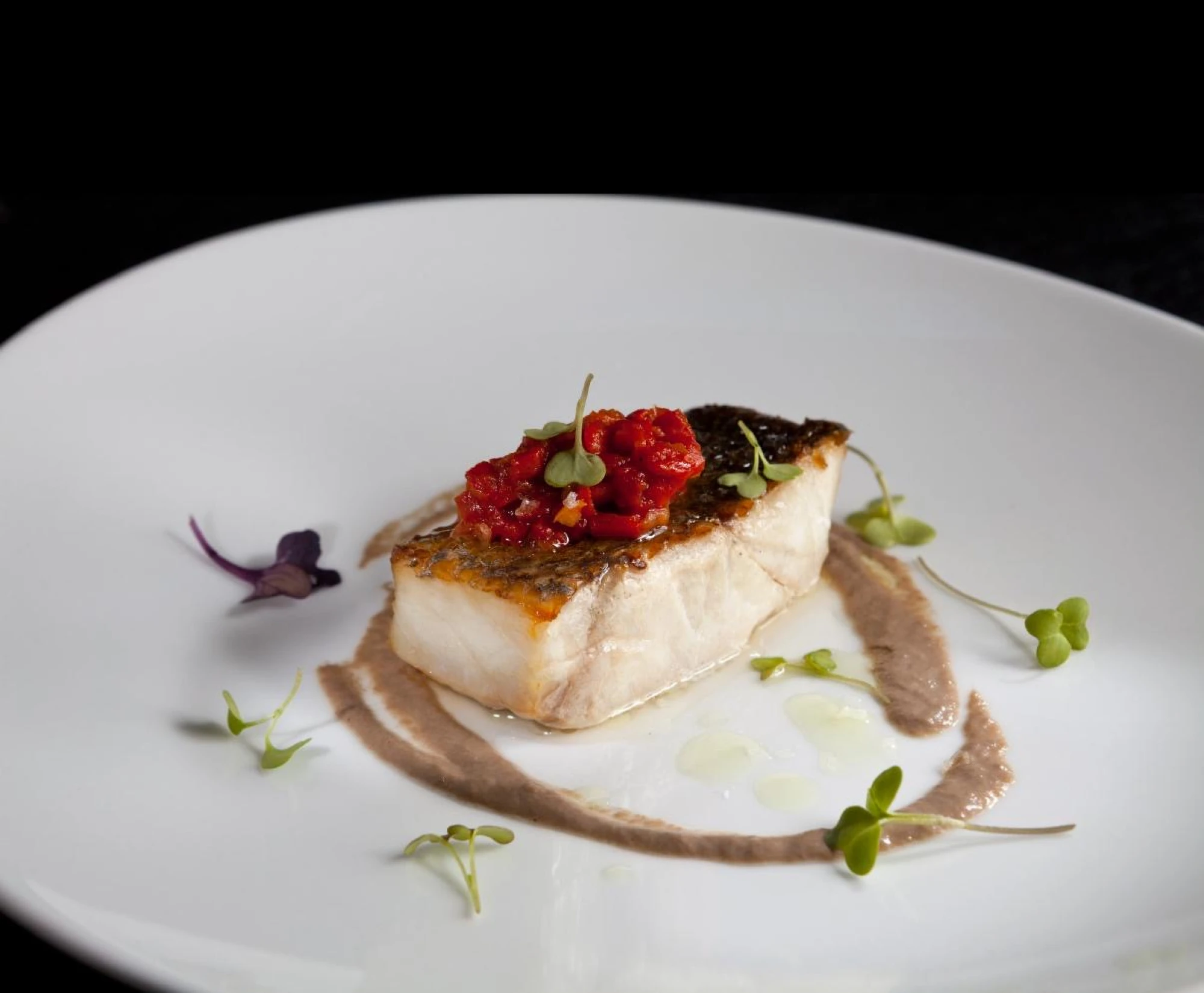 Plato de corvina presentado con una confitura de piquillos y tomate, acompañado de una suave muselina de setas, en una presentación elegante y apetecible.