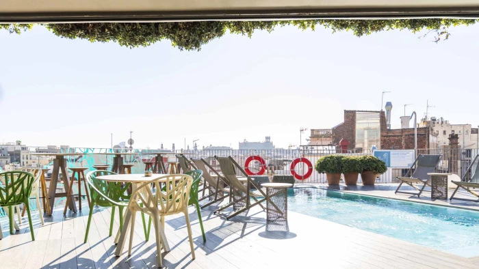 Se ve una terraza con sillas y una piscina al aire libre junto a una vista urbana.