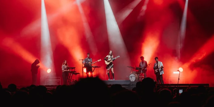 Un gruppo musicale si esibisce su un palco con luci rosse e attrezzatura tecnica visibile.