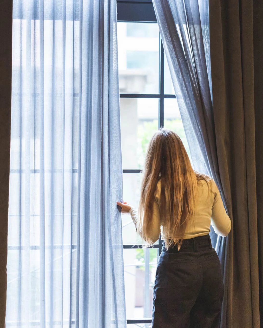 Una persona está de pie junto a una ventana con cortinas abiertas.