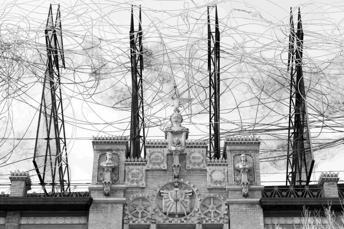 A stone façade with sculptures and an installation of black wires stands out against the cloudy sky.