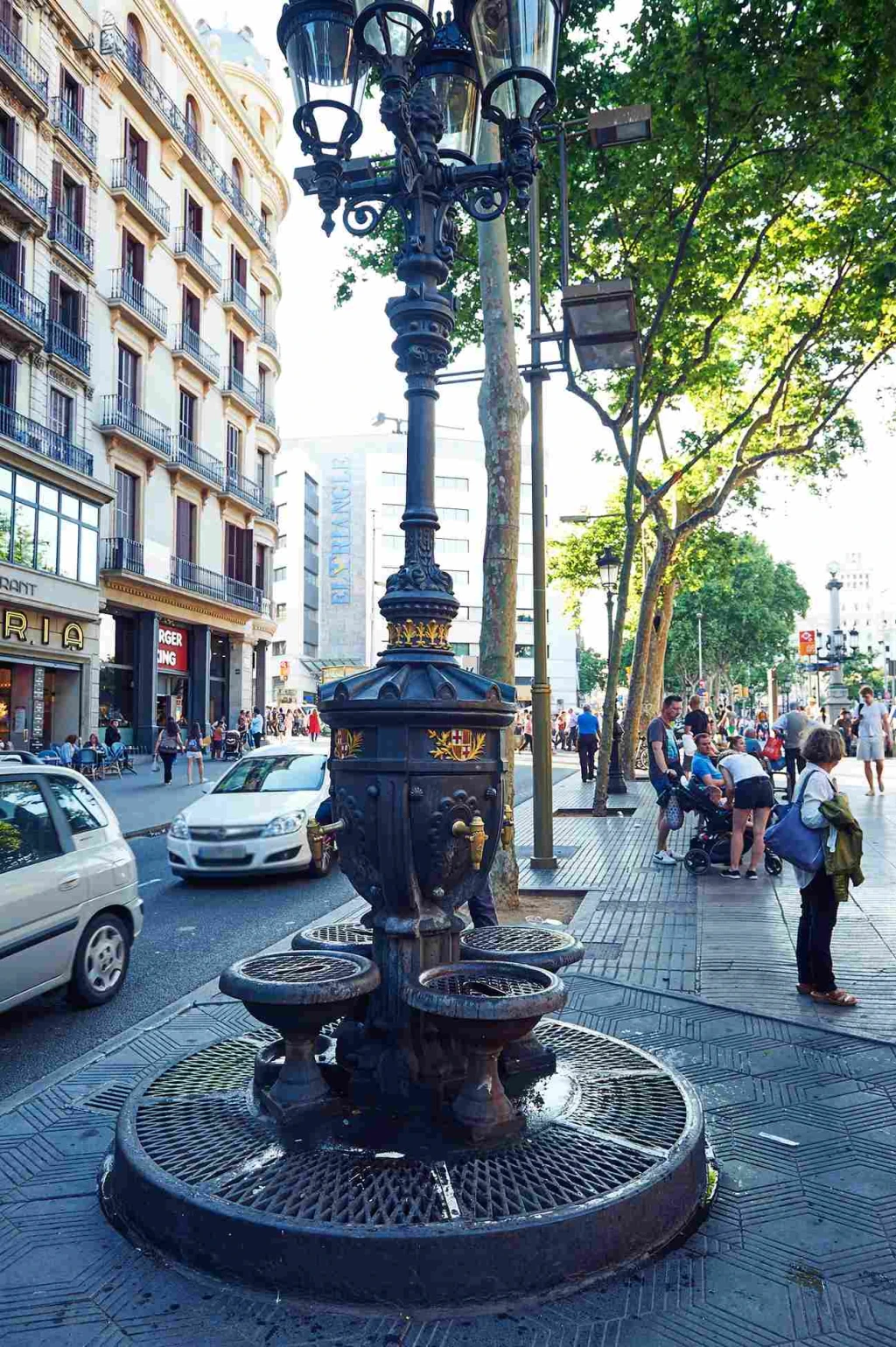 Se ve una farola decorativa de hierro en una acera junto a edificios y peatones.