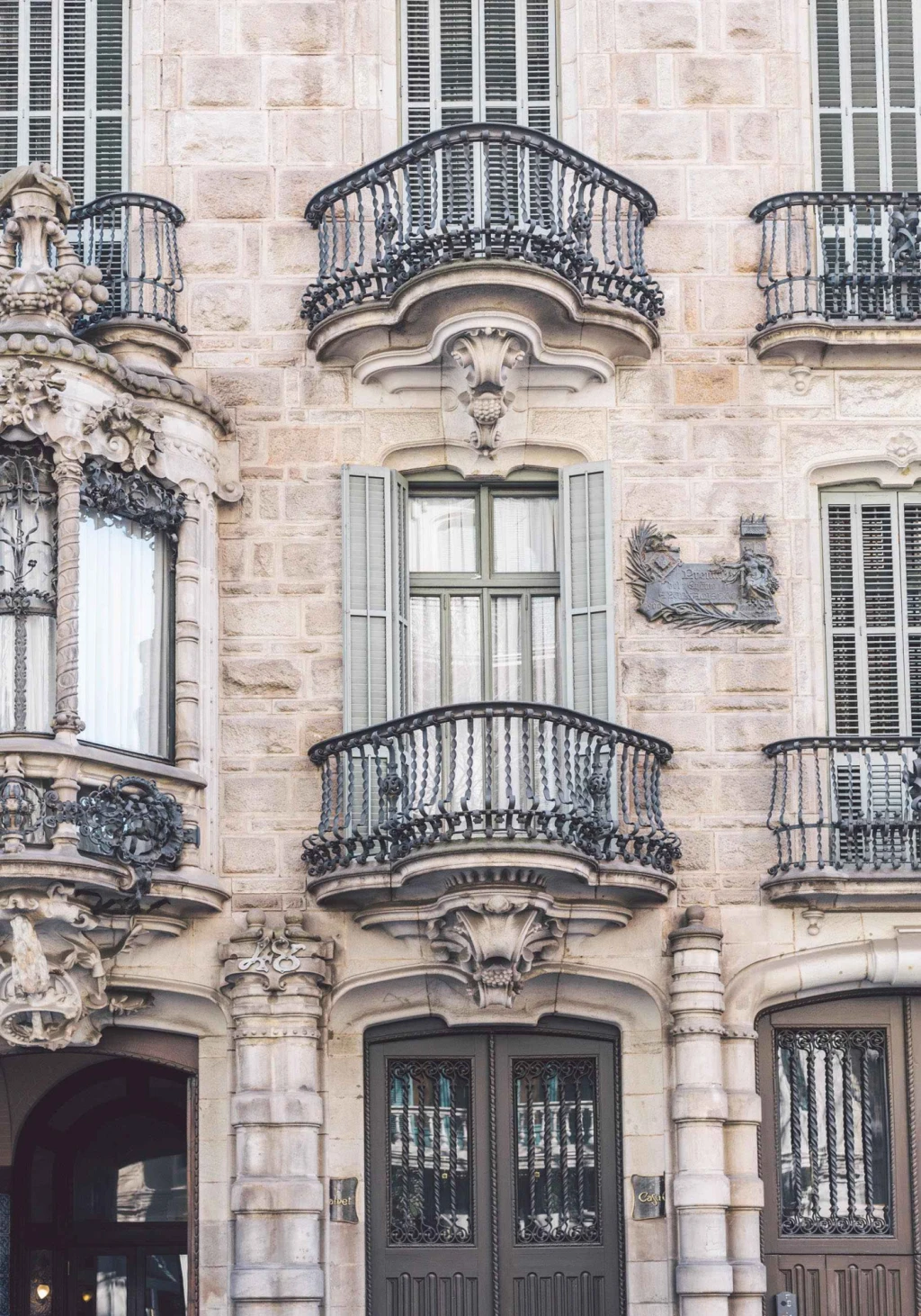 On voit une façade en pierre avec des balcons en fer et des fenêtres aux encadrements décoratifs.