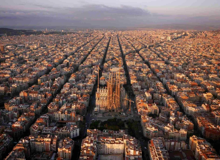 Se ve un panorama urbano del Eixample con calles largas y edificios densos bajo un cielo nublado.
