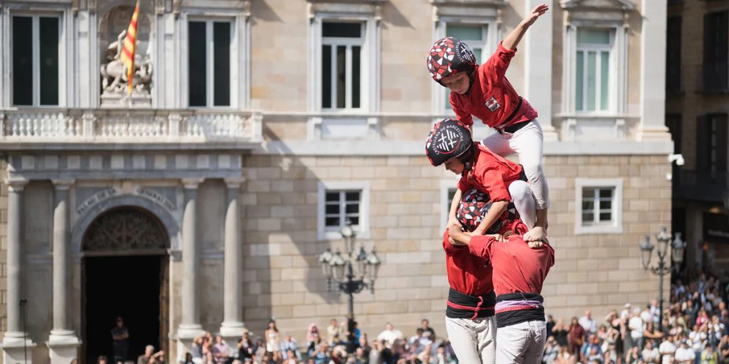 Une personne vêtue d’un costume rouge et un groupe dansant lors d’un défilé en plein air avec des bâtiments en arrière-plan.