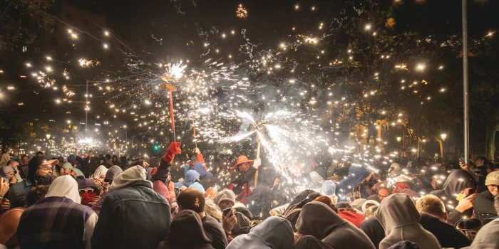 La scène montre un groupe de personnes dans la rue, avec des étincelles et de la fumée qui illuminent l’ambiance nocturne.