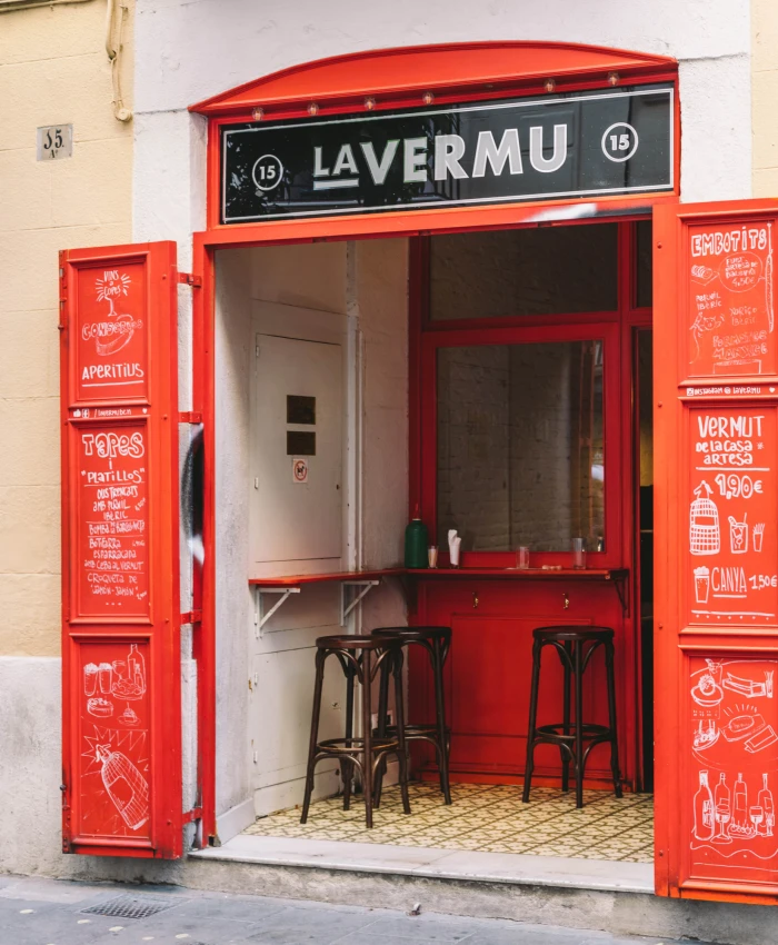 Un bar acogedor con una decoración moderna y cálida, que presenta una barra de madera y estanterías con botellas de bebidas, creando un ambiente invitador para los clientes.