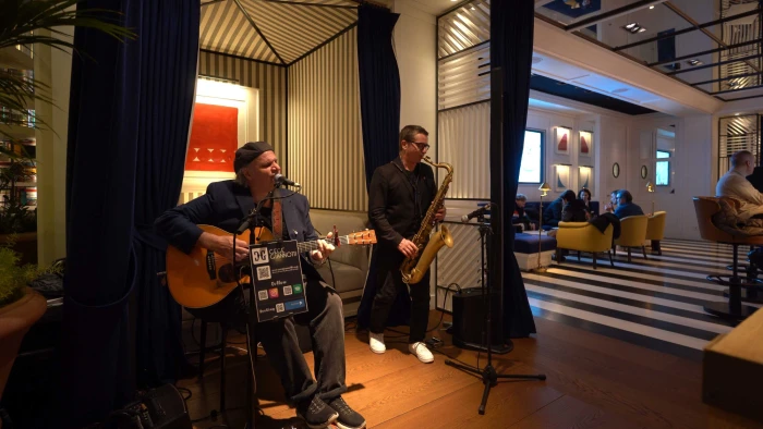Se ve un escenario con músicos y equipo de sonido en una sala con asientos y luces decorativas.