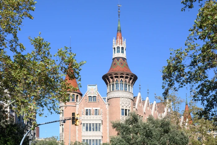 A modernist brick-and-ceramic tower with a dome is visible, surrounded by trees under a blue sky.