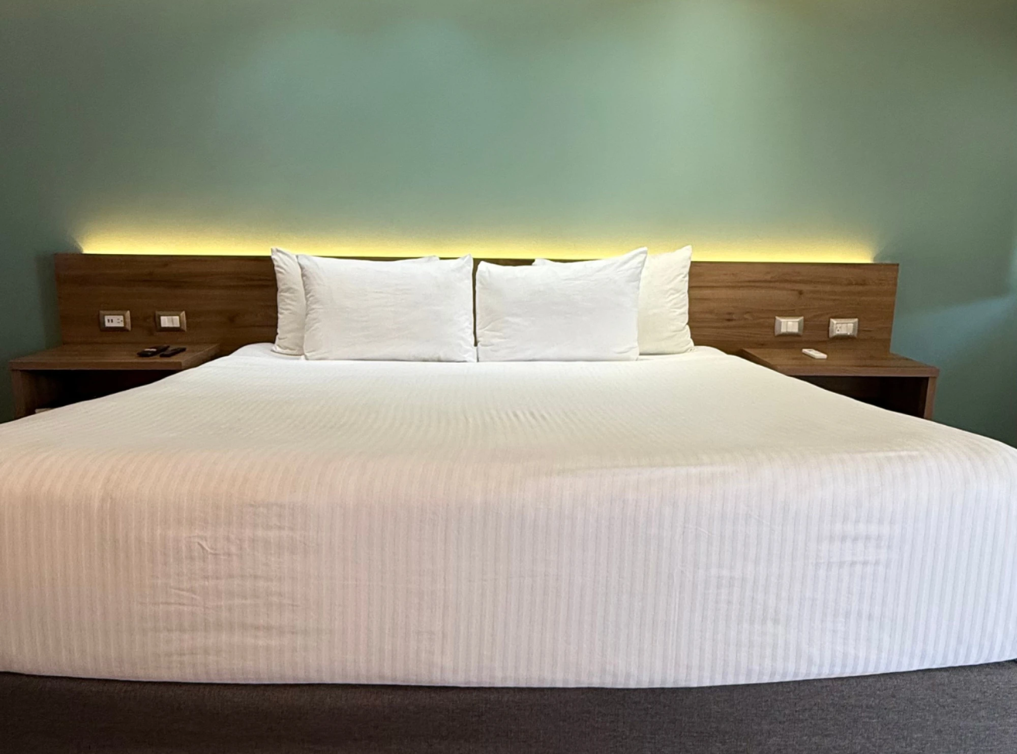 Se ve una cama doble con ropa de cama blanca y dos almohadas sobre una base de madera en un dormitorio.