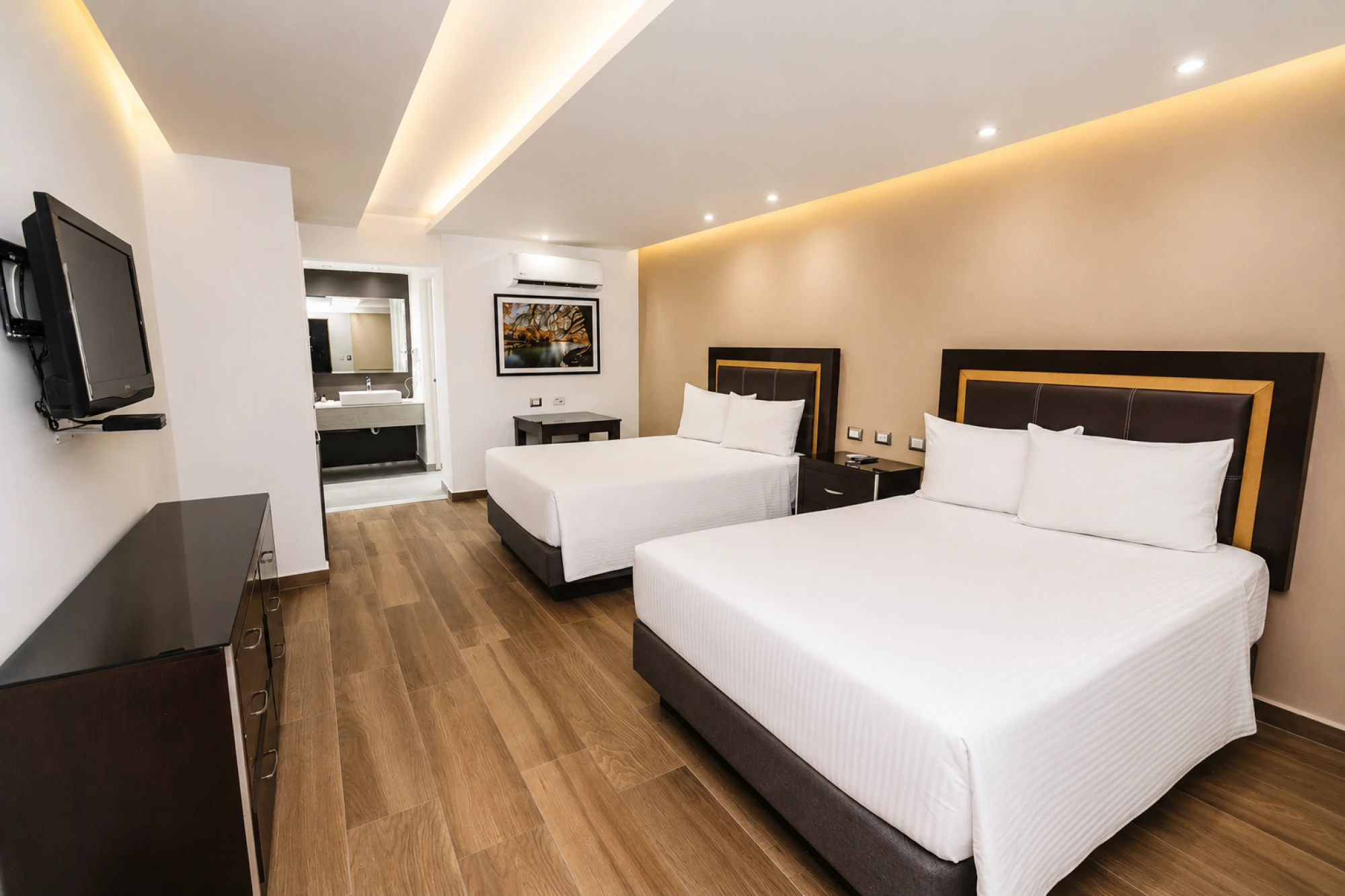 Se ven dos camas individuales con ropa de cama blanca, una televisión de pared y un escritorio en la habitación.