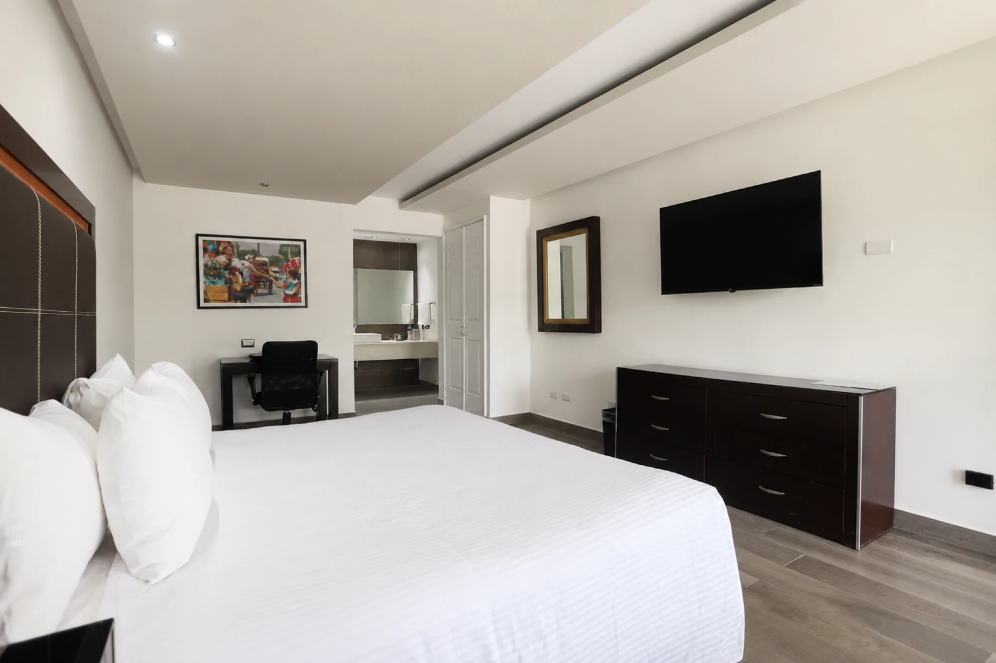 Se ve una cama con ropa de cama blanca, una televisión de pantalla plana y un escritorio en la habitación.