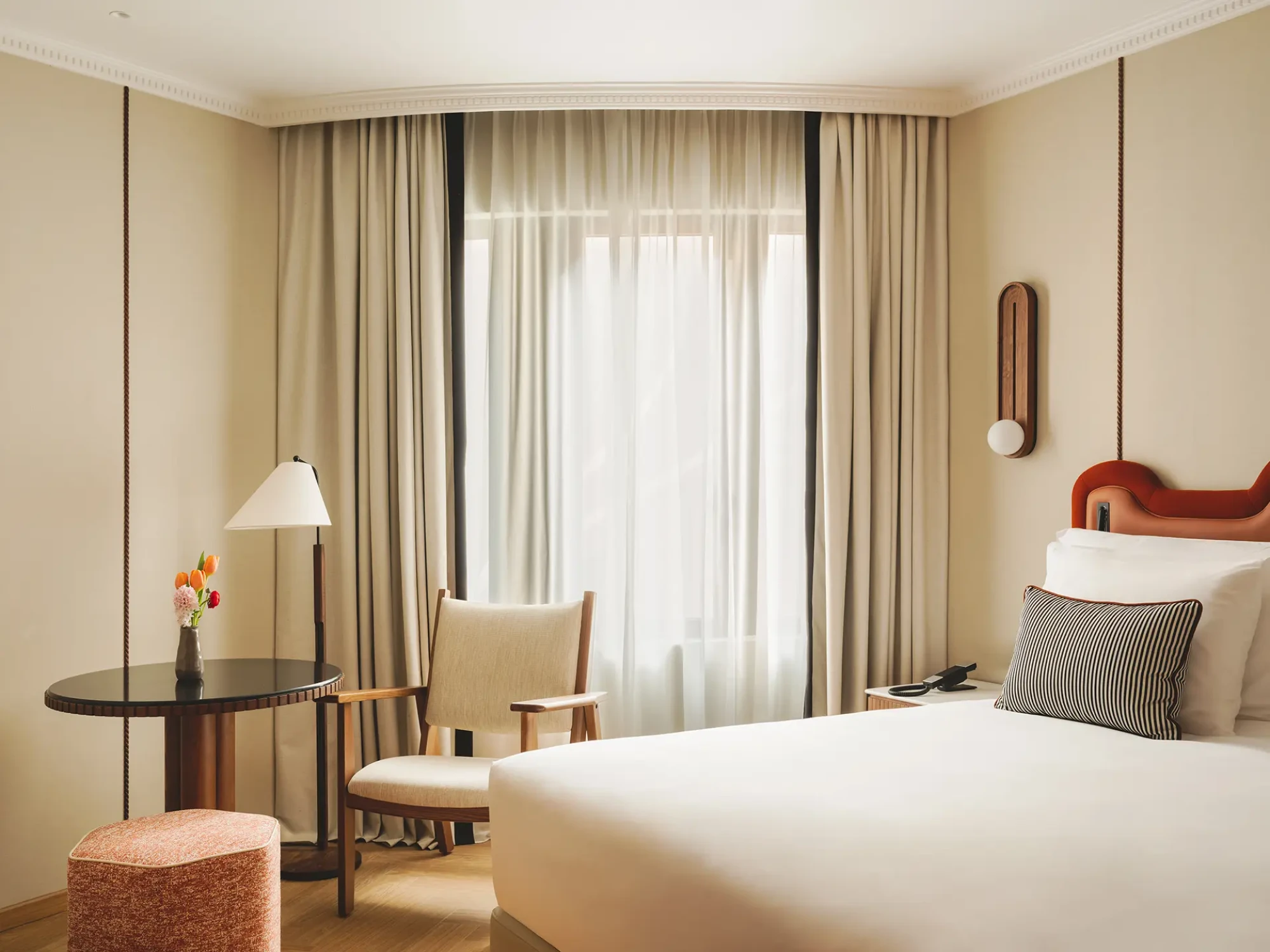 Se ve una cama con almohadas, cortinas claras y una lámpara de pie en la habitación.