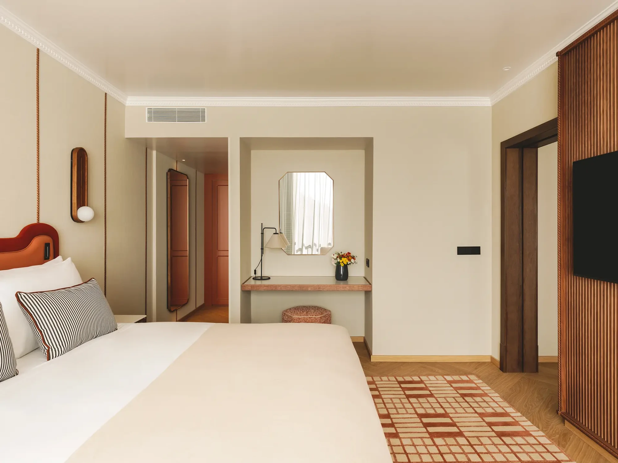 Se ve una cama doble, una zona de estar y un tocador con espejo en una suite.