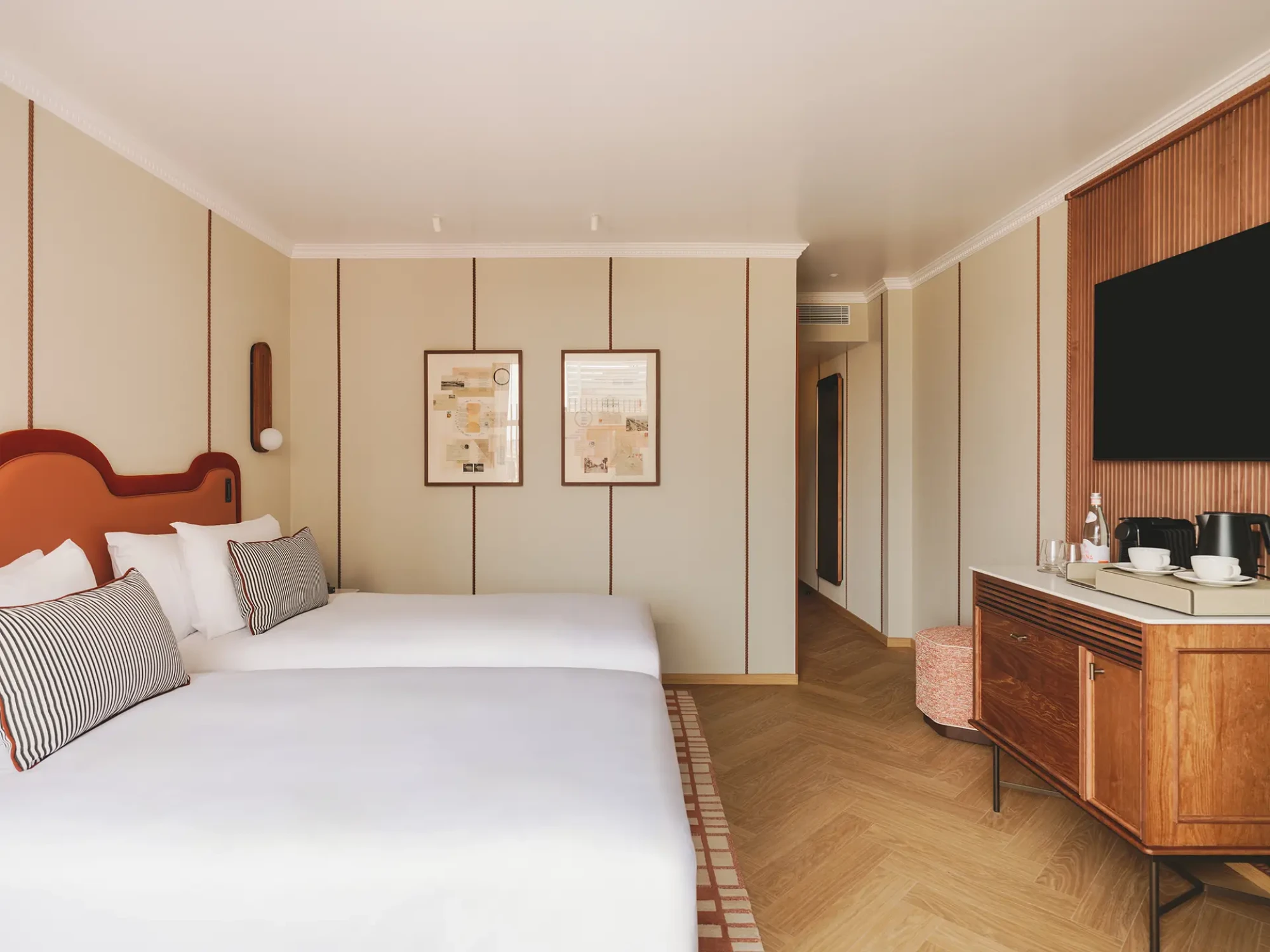 Se ve una cama con almohadas, un cabecero con cuadros y un tocador con lavabo en la habitación.
