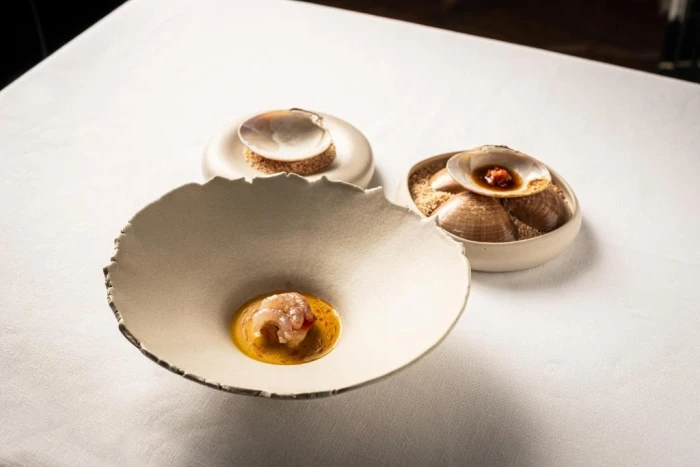 Se ve un plato con un bocado y dos cuencos pequeños sobre una mesa con mantel claro.