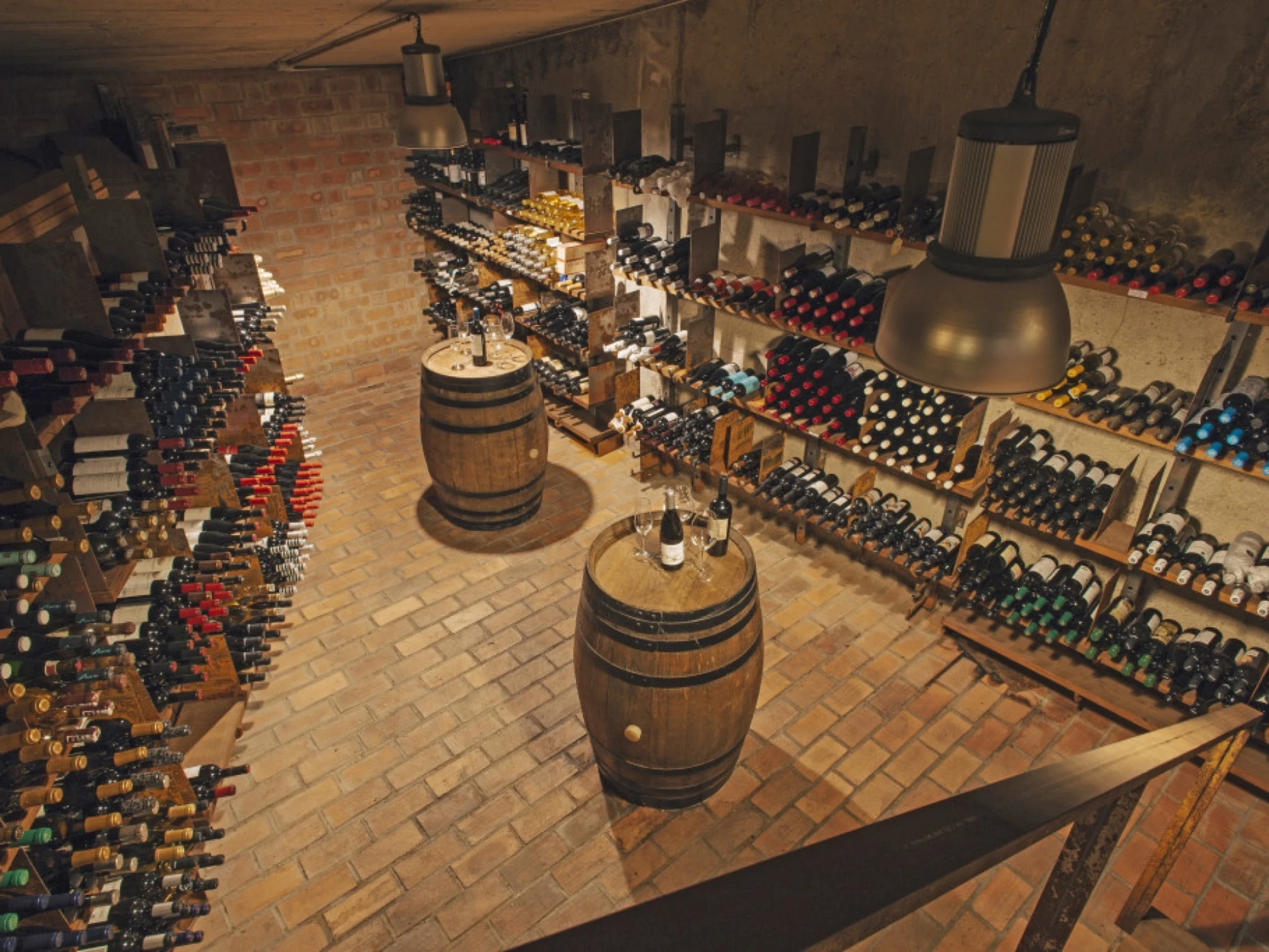 Se ve una sala de cava con barricas de madera y estanterías llenas de botellas de vino.