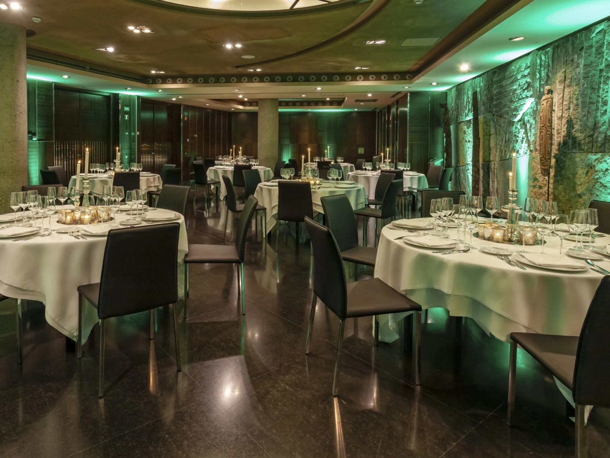 Salón de banquetes con mesas cubiertas con manteles blancos y sillas negras, iluminado con luces verdes.