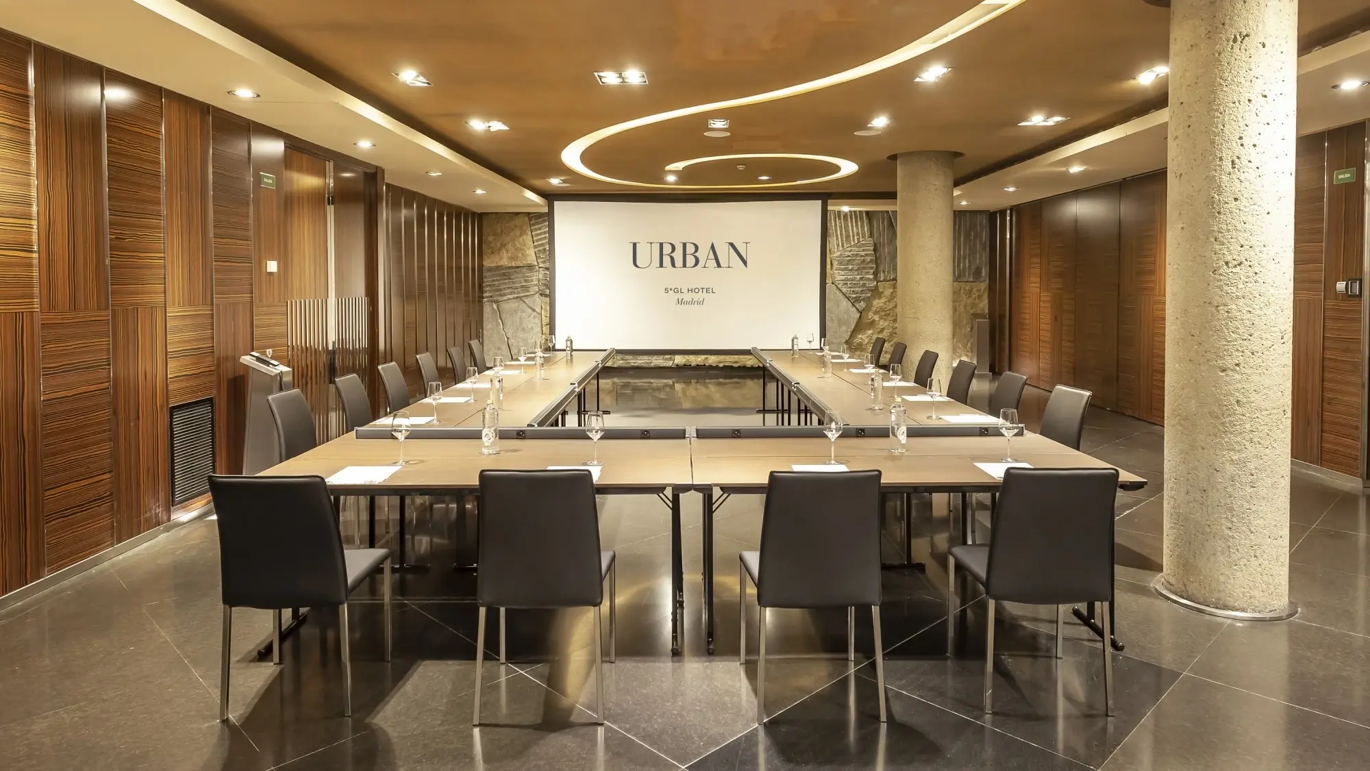 Se ve una sala de reuniones con una mesa larga, sillas y un mostrador al fondo.