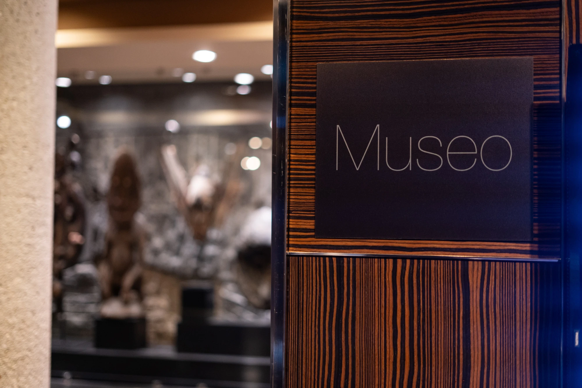 Se ve un letrero con la palabra “Museo” junto a una pared de madera y un espacio interior al fondo.