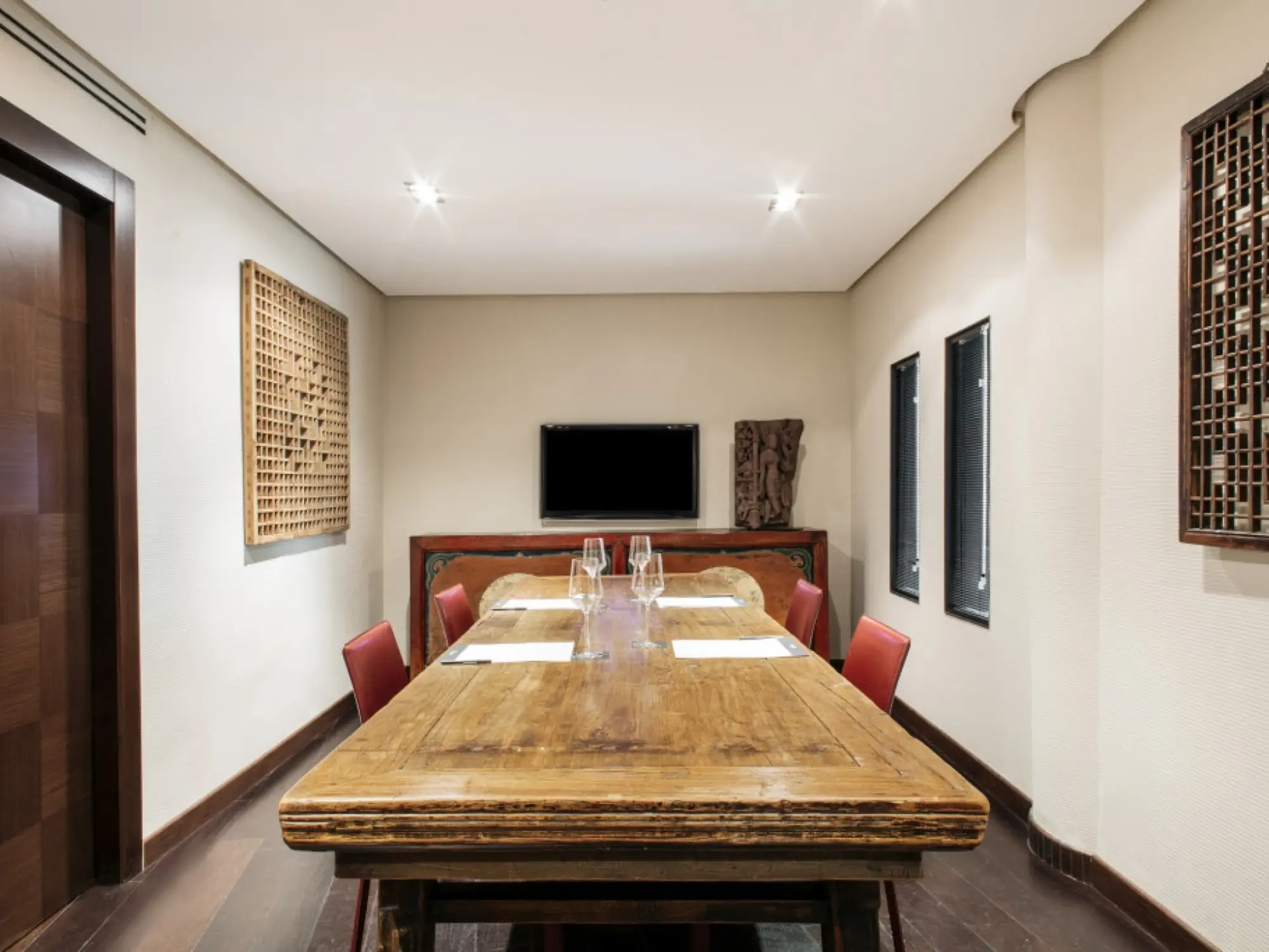 Se ve una sala con una mesa de madera y sillas alrededor, además de cuadros y una televisión en la pared.