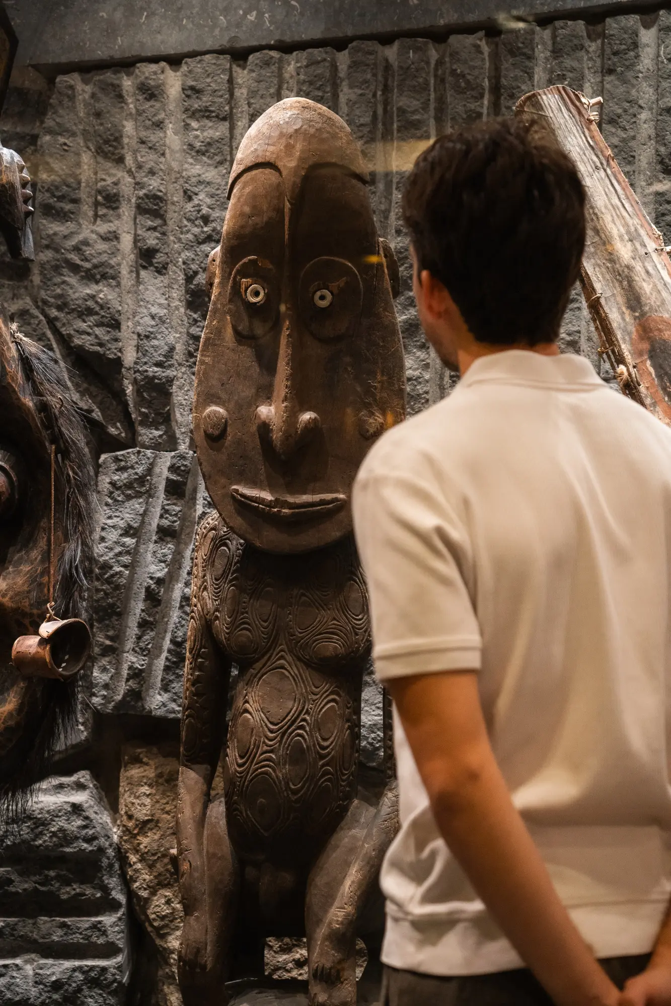 Una persona observa una escultura decorativa de estilo figurativo junto a una pared de piedra.