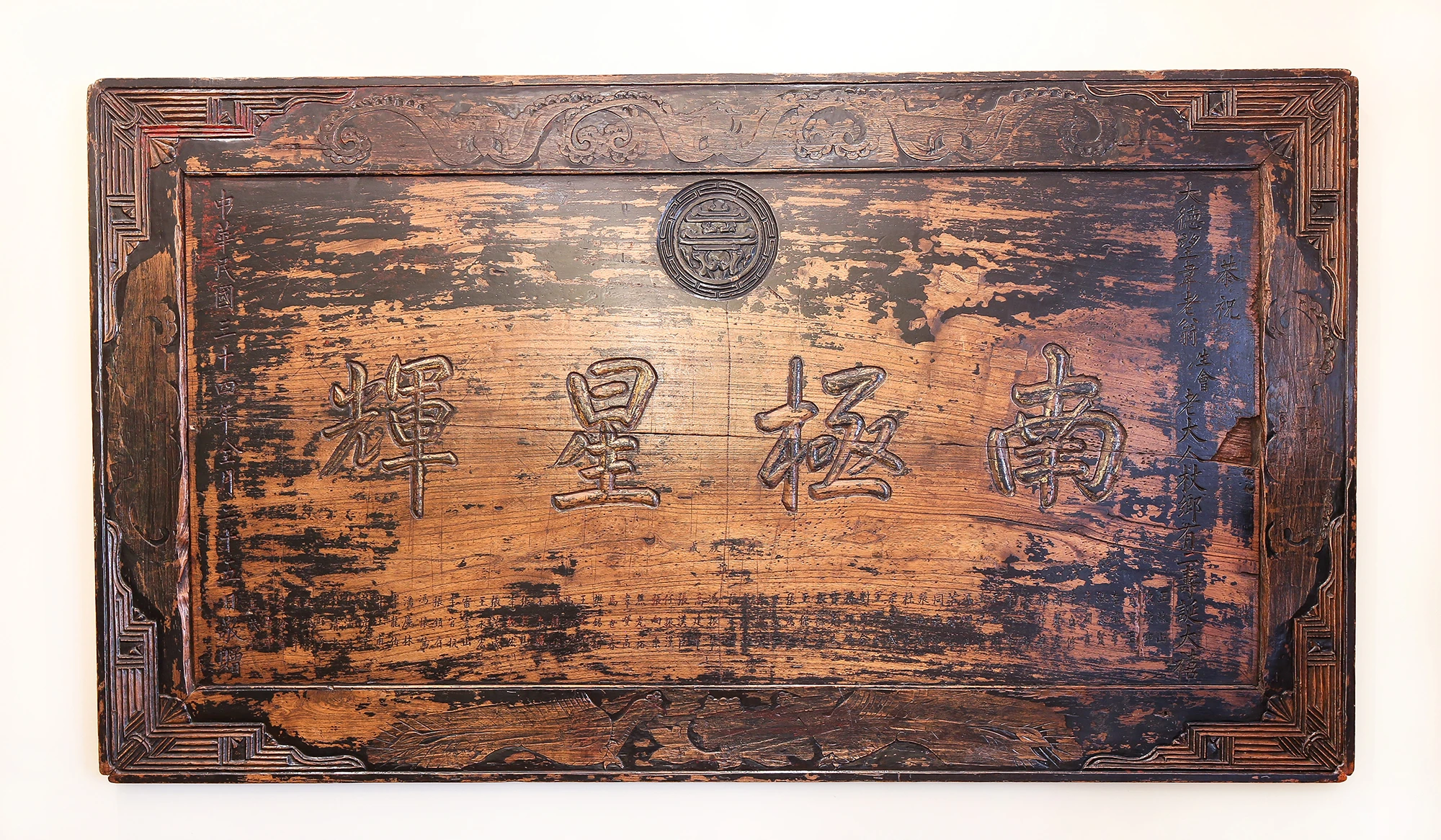 Se ve un cuadro decorativo de madera con inscripciones y un emblema central en la pared.