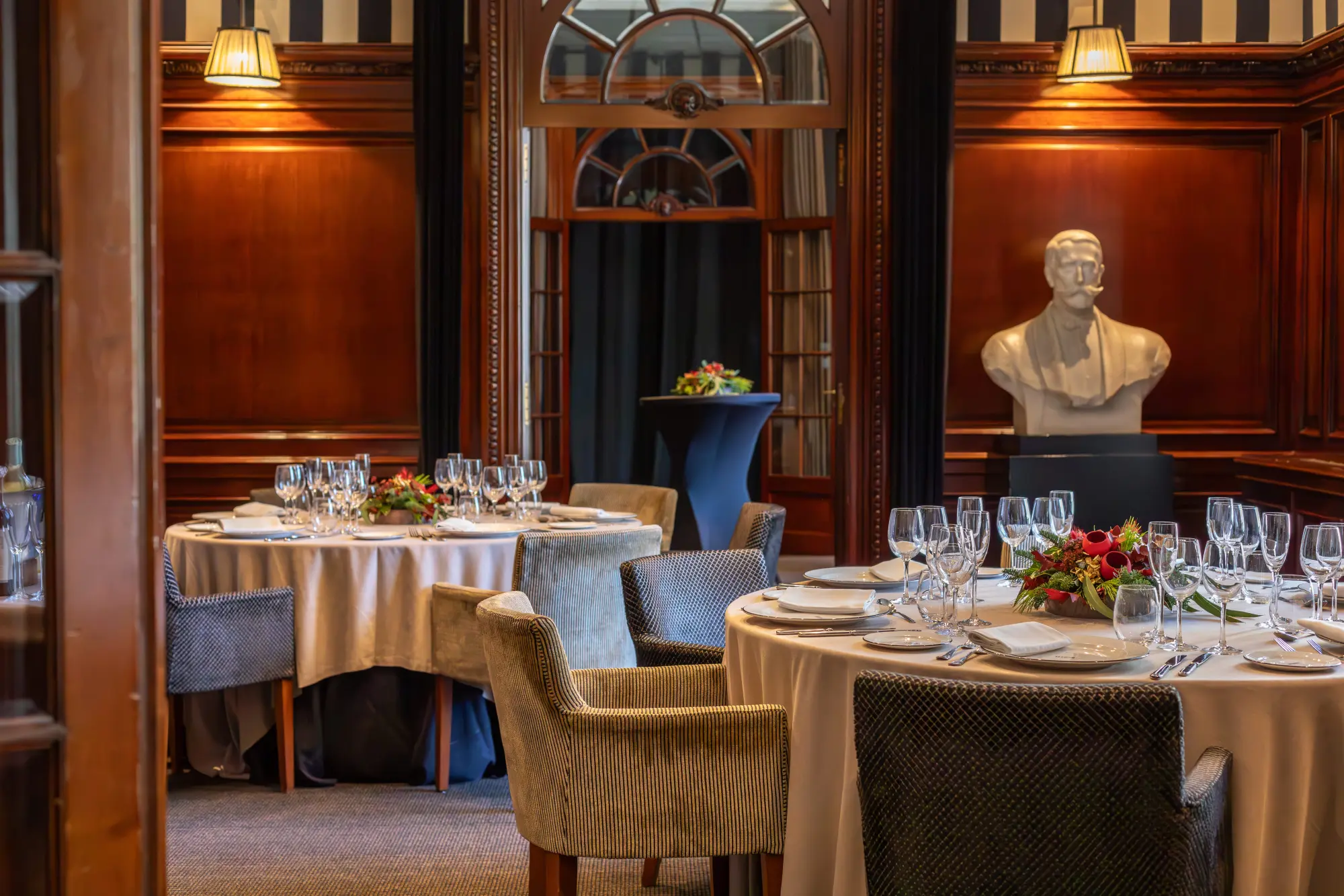 Se ve un comedor con mesas cubiertas, sillas tapizadas y decoración floral sobre la mesa.