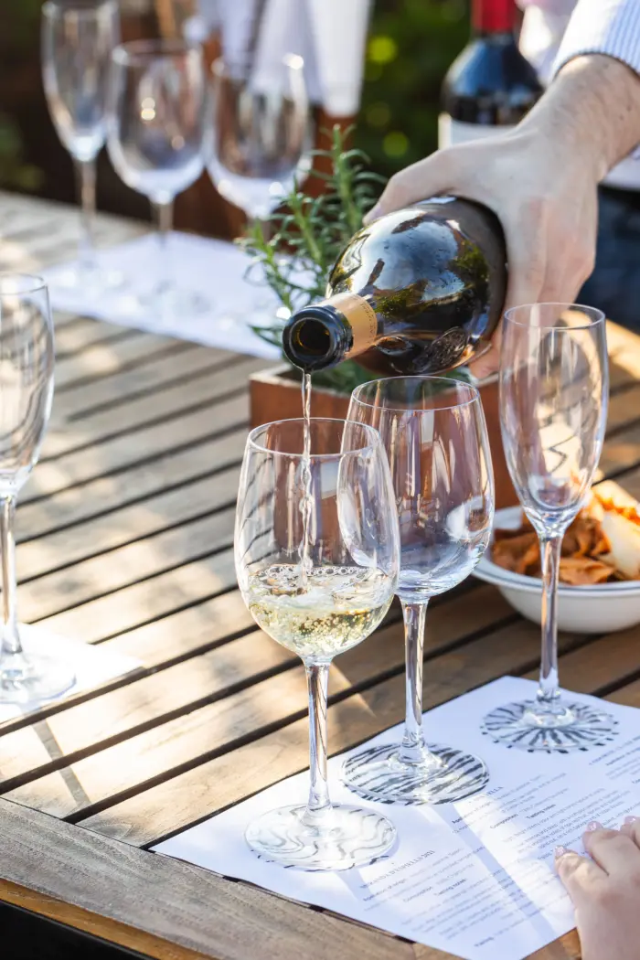 Wein wird aus einer Flasche in Gläser auf einem Tisch mit weißer Tischdecke eingeschenkt.