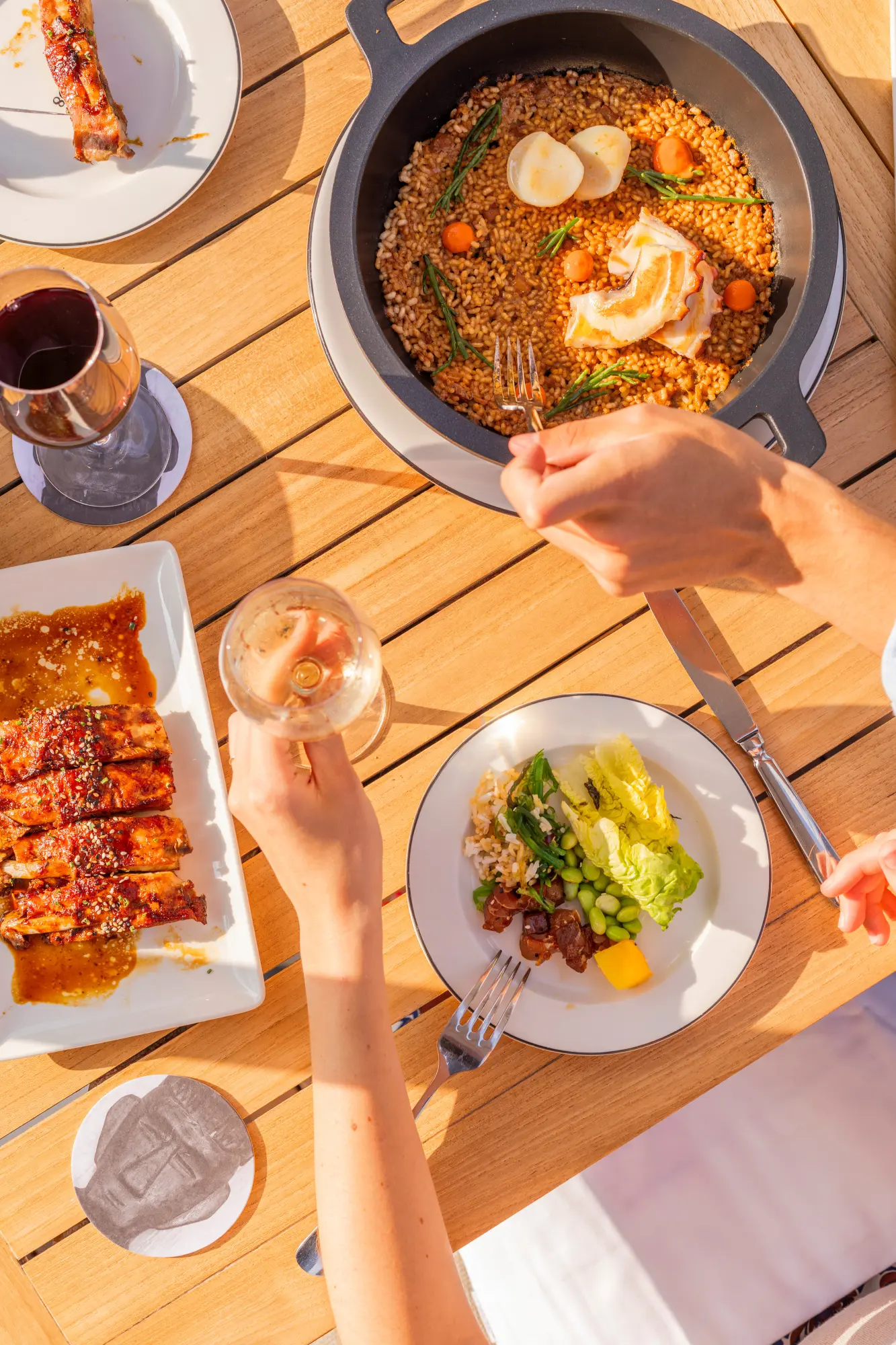 Ils servent des brochettes de fruits de mer sur un plateau avec un bol de sauce et une pizza en arrière-plan.