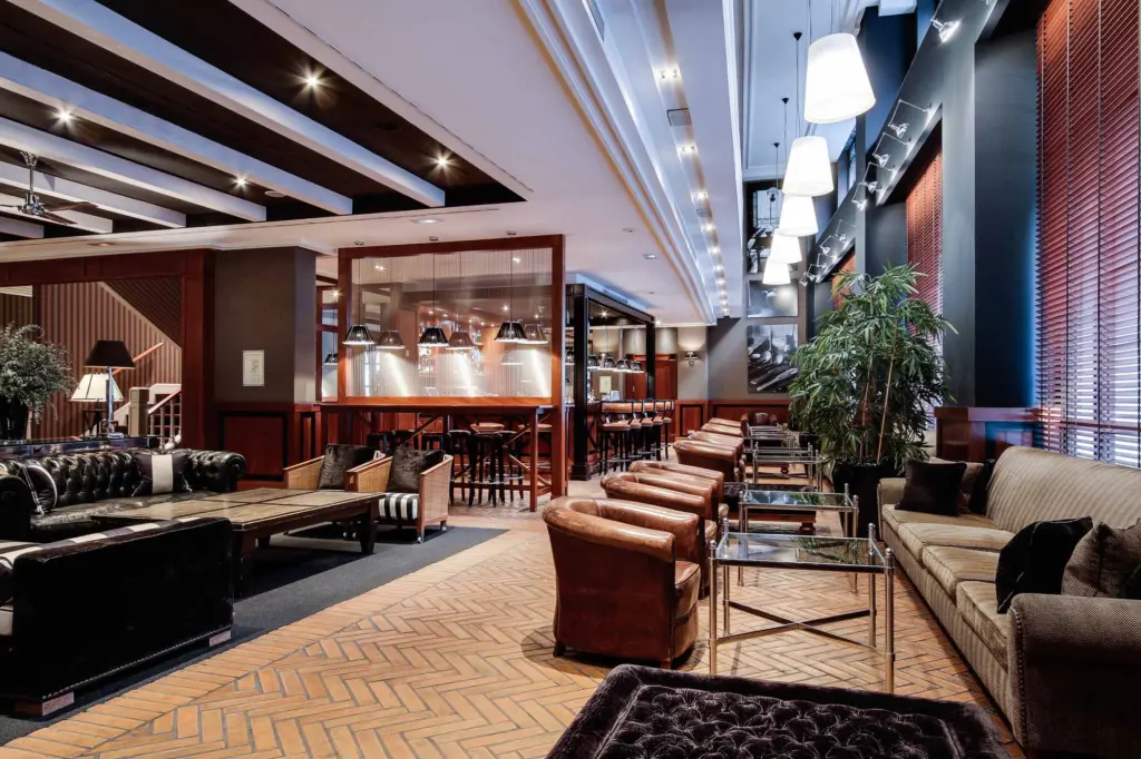 The bar features leather seating, tables, a lit counter, and decorative plants inside.