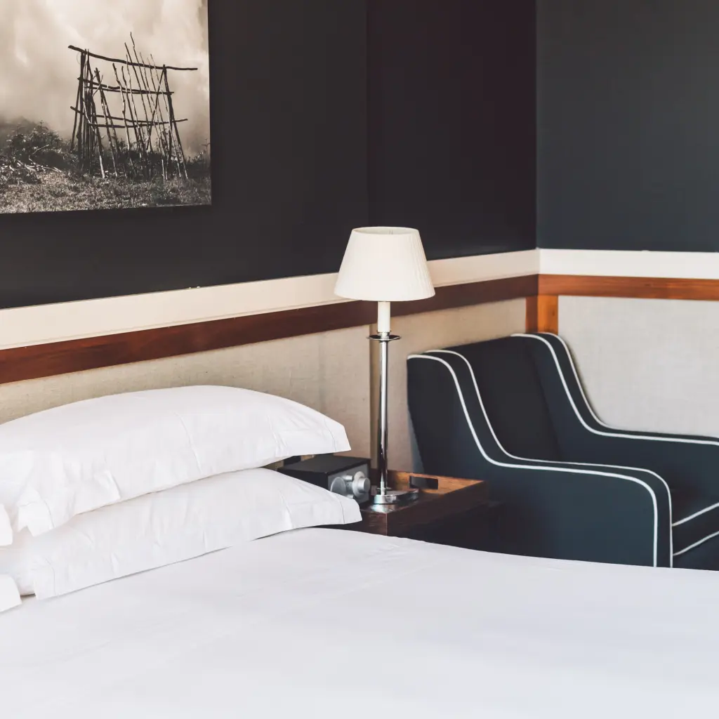 Si vede un letto con cuscini, un divano e una lampada da tavolo su un comodino.
