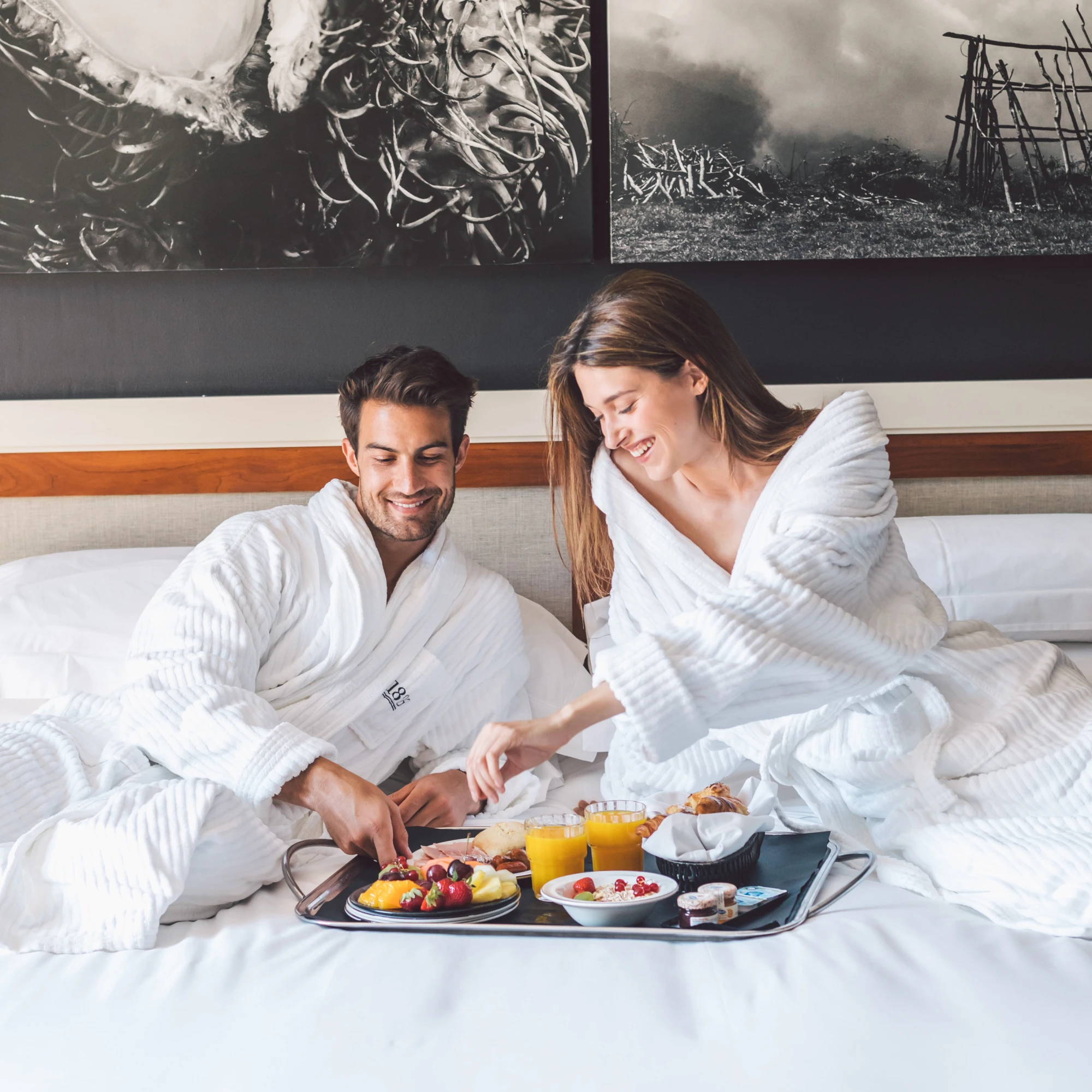 Una coppia fa colazione su un vassoio su un letto con lenzuola bianche.
